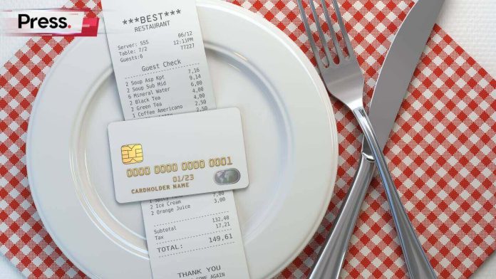 Restaurant receipt bill in white china plate and payment card stack on it with cutleries of fork and spoon beside on checkered red white table cloth
