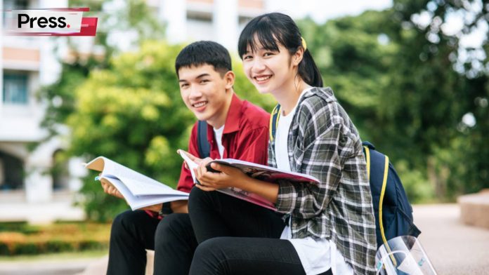 Two happy campus students looking at the camera, one male and one female, dressed casually while holding their books. They are happy because they know the Malaysia higher education plan for 2026-2035 will benefit them as well as many others.
