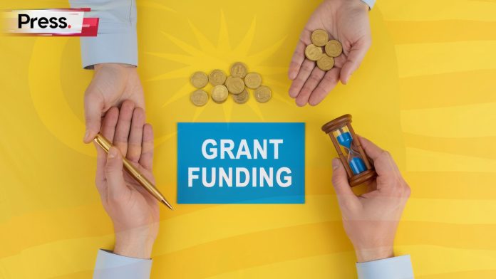Press. logo top-left; three hands around a blue card reading ‘GRANT FUNDING’—one with coins, one with a pen, one with an hourglass—on a yellow background with the Malaysian flag motif.