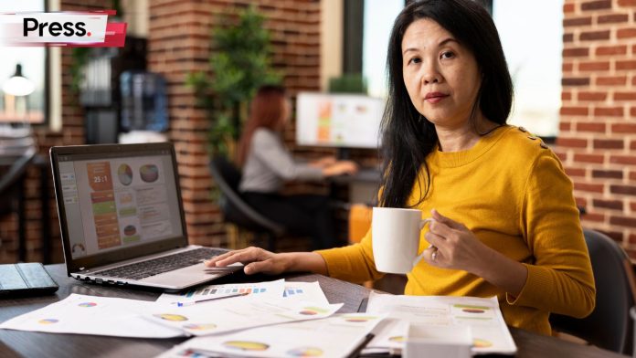 A Malaysian SME owner reviewing digital invoices on a laptop with business documents, calculator, and coffee nearby.