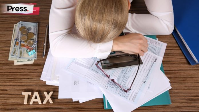 Exhausted woman resting on tax documents and calculator with cash nearby, symbolising deferred tax stress.