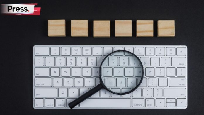 A photo of a computer keyboard with an hourglass lying on top of it. There is a series of 6 wooden blocks placed in a row above the keyboard. The magnifying glass and keyboard are symbolic of a keyword audit.