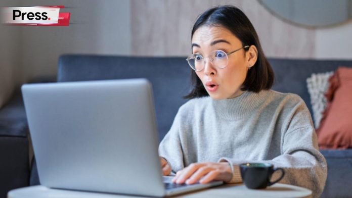 A shocked bespectacled woman sits at her computer typing and researching keyword difficulty.