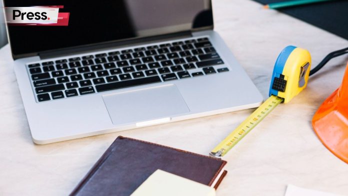 A photo of a workdesk with various items on top of it. The items are a laptop, a measuring tape, and a closed notebook. The measuring tape represents the measuring of on page SEO.