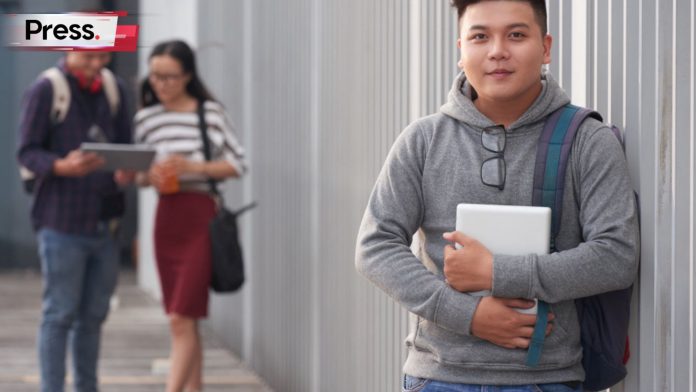 Three students are in the picture, a boy and girl in the background and another boy in the front. The two students in the background are discussing something, possibly how to select the right pre university course in Malaysia.
