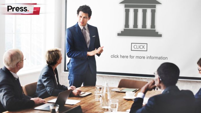 A well-dressed man stands in front of a room of other professionals, presenting his topic on the screen. He is talking about authority, which ties in to page authority.