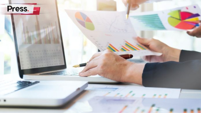 A photo of a person working at their laptop, holding documents as they do a SEO competitor analysis,