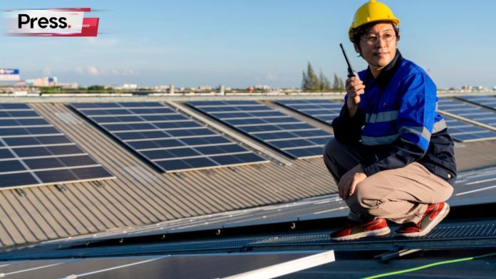 A construction worker squats next to a row of solar panels, holding a screwdriver. This is symbolic of Malaysia's Solar ATAP program.