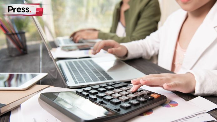 Business officer typing on laptop while calculating using calculator.