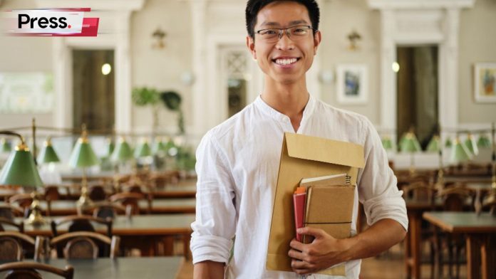 A male student in a twinning programme smiles, holding his file and notebooks.