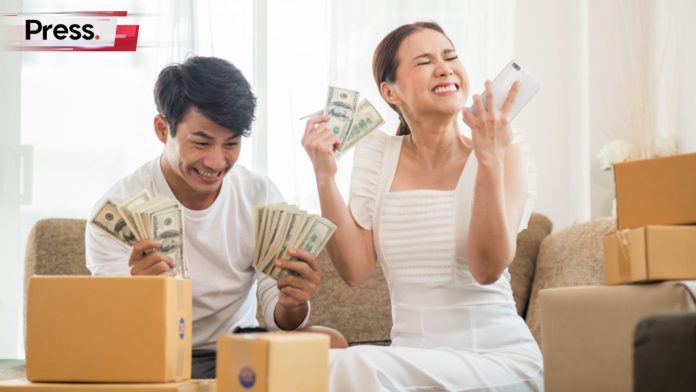A couple going crazy as they hold money in their hands. They are also surrounded by boxes in their living room, symbolizing lifestyle inflation.