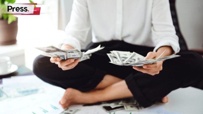 A woman sits cross-legged in a meditative pose, holding large bundles of money in her hands. This symbolizes passive income.