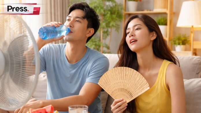Malaysian couple cooling off indoors with fan, drinking water, and eating watermelon during hot weather.