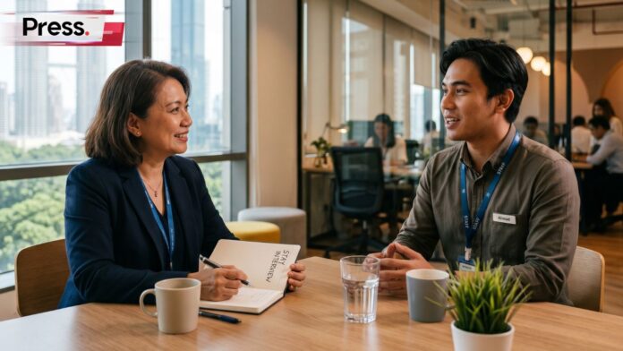 An HR manager and male employee conducting a stay interview in a Kuala Lumpur office with Twin Towers background.