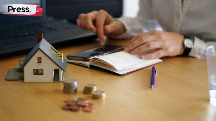 Photo of a person calculating money with a model house and coins on the desk in front of them, representing a person searching for mortgage consultants.